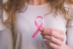Middle aged woman holds a pink ribbon in front of her newly reconstructed breasts after breast cancer
